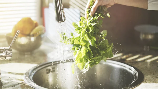 En kvinna tvättar grönska neetle mint i köket — Stockfoto