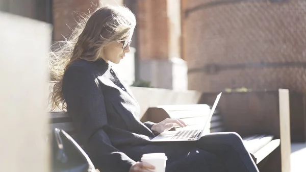 Ragazza seria in occhiali, caffè, notebook, panchina — Foto Stock