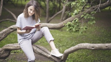 Gülümseyen bir esmer beyaz kız parkta bir kitap okuyor