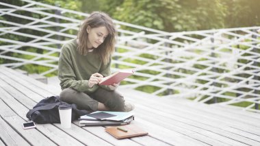 Gülümseyen kız açık havada bir kitap okuma merdivenlerde oturuyor