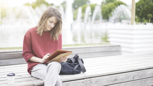 Una giovane ragazza carina seduta nel parco con un tablet — Foto Stock