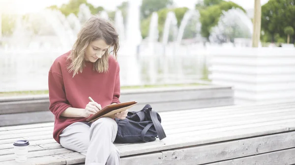 Una giovane ragazza carina seduta nel parco con un tablet — Foto Stock