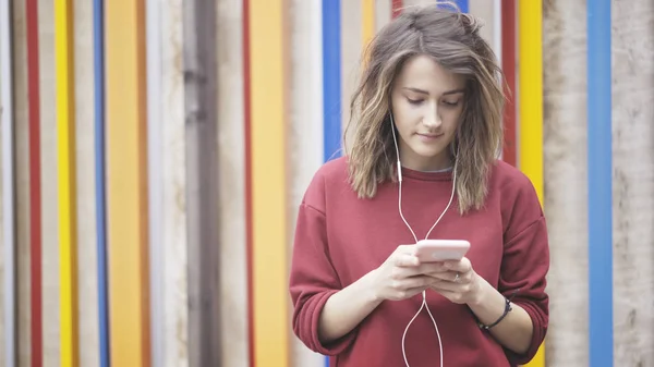 Een jong meisje luistert naar muziek in oortelefoons op de achtergrond van de cloured — Stockfoto