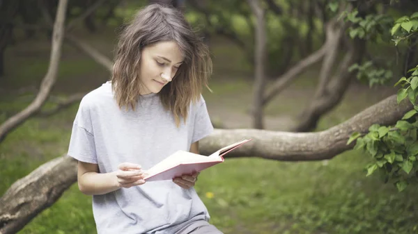 Una ragazza bruna sta leggendo un libro nel parco — Foto Stock