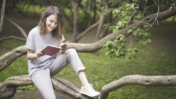 Uma menina branca morena rindo está lendo um livro no parque — Fotografia de Stock