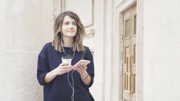 Een lachende brunette wit meisje luistert naar muziek buitenshuis — Stockfoto