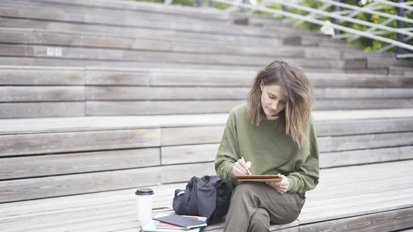 Una ragazza è seduta sulle scale a lavorare con un tablet — Foto Stock