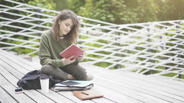 Uma menina está sentada nas escadas lendo um livro ao ar livre — Fotografia de Stock