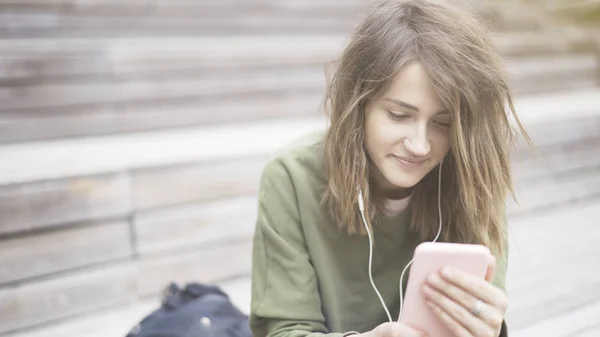 Een close-up van een jonge lachende mooi meisje houdt van een telefoon luisteren naar muziek — Stockfoto