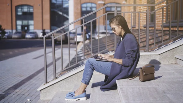 Een jong meisje in zonnebril is werken met een laptop outisde — Stockfoto