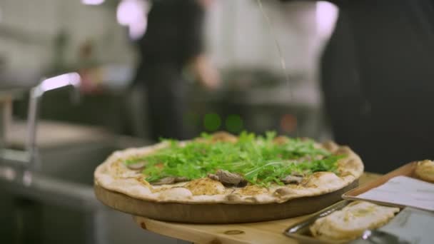 Шеф-повар добавляет оливковое масло в готовую пиццу ручной работы с арогулой — стоковое видео