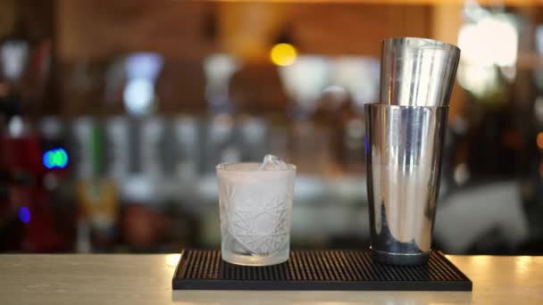 Close up pan shot of crystal glass with ice and metal shaker in bar — Stock Video