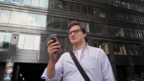 Pan shot van de mens scrollen de telefoon op de achtergrond van glas ramen — Stockvideo