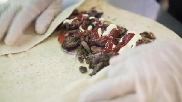 Handheld shot van chef-kok handen in witte handschoenen rollen rundvlees doner in pita — Stockvideo
