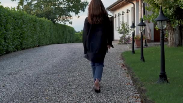 Eingesperrte Echtzeitaufnahme einer jungen Frau, die den Pfad auf dem Territorium einer schönen Villa entlanggeht. — Stockvideo