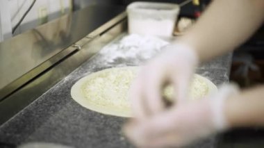 Elle tutulan aşçı peynirli pizzanın üzerine siyah zeytin koyuyor.