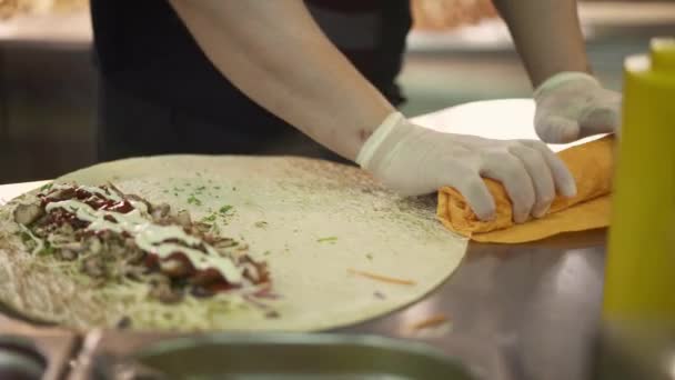 Handheld schot van chef-kok handen in witte handschoenen rollen twee donateurs in pita — Stockvideo