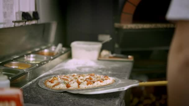 Handheld shot van kok het nemen van een zeevruchten pizza te bakken in de oven — Stockvideo