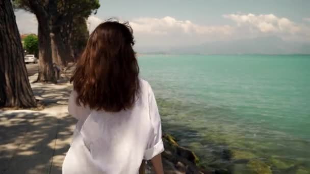 Echtzeit-Portraitaufnahme eines jungen schönen Mädchens, das am Ufer des Gardasees entlang geht. — Stockvideo