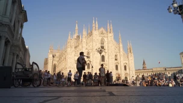 ミラノ,イタリア- 2019年7月:ドゥオーモ・ディ・ミラノを背景にギターを弾く男の手持ち撮影 — ストック動画