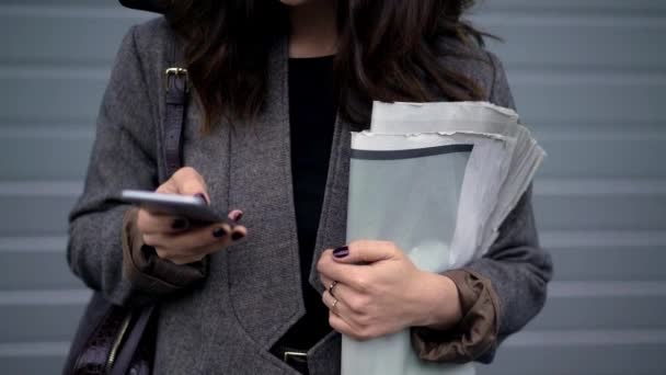 Pan shot of woman holding newspapers and typing in the phone — Stock Video