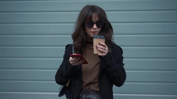 Langzame beweging van de vrouw in een zonnebril met telefoon en een kopje koffie — Stockvideo