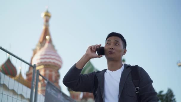 Valós idejű portré egy fiatal ázsiai fickóról, aki telefonon beszél Moszkva közepén.. — Stock videók