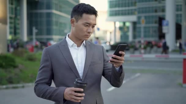 Realtidsfotografering av en ung affärsman, ledande korrespondens på telefon med kaffe i händerna. — Stockvideo