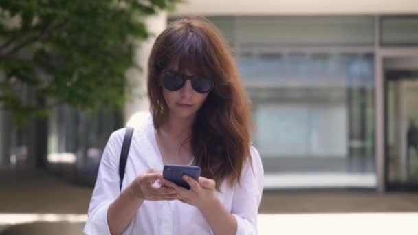 Gimbal shot of woman texting on the phone walking along the road — 비디오