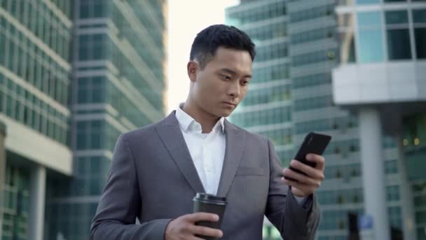 Portrait en temps réel de gauche à droite d'un jeune homme d'affaires, correspondance au téléphone avec café dans les mains . — Video