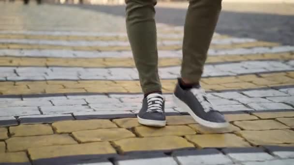 В реальном времени крупным планом снимают парня, идущего по переходу в зеленых джинсах и кроссовках — стоковое видео