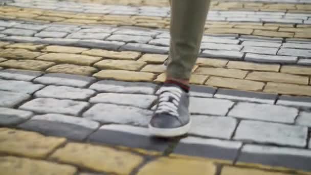 Yeşil kot ve spor ayakkabılarla yaya geçidinde yürüyen bir adamın yakın çekim görüntüsü.. — Stok video