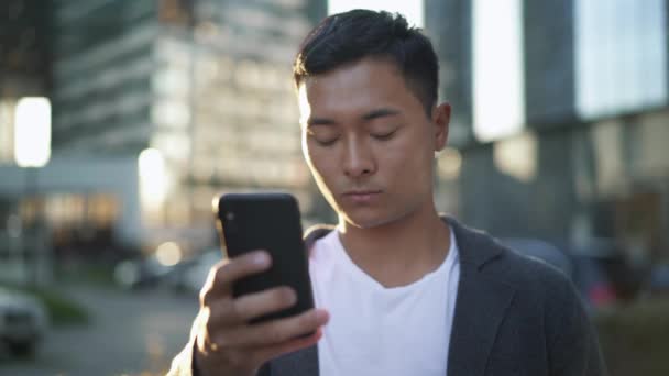 Realtids porträtt av en ung asiatisk man som står på gatan och leder en korrespondens på telefon — Stockvideo