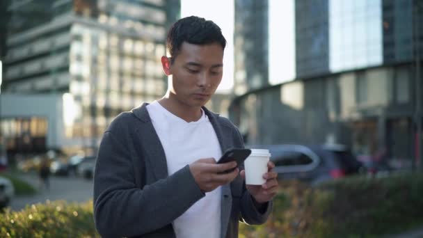 Poêle gauche à droite prise de vue en temps réel d'un homme textant au téléphone et buvant du café . — Video