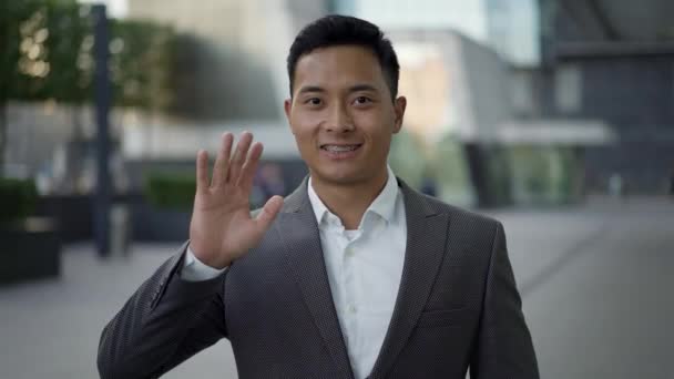 Gülümseyen ve el sallayan Asyalı genç bir iş adamının gerçek zamanlı portresi. — Stok video