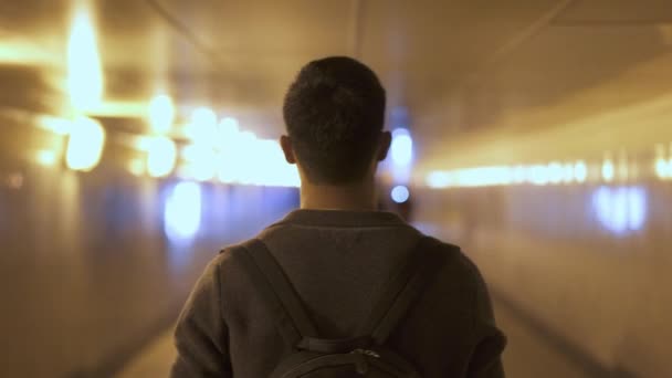 Porträtt i realtid av en ung asiatisk man som går längs en upplyst gångtunnel. Bakifrån — Stockvideo