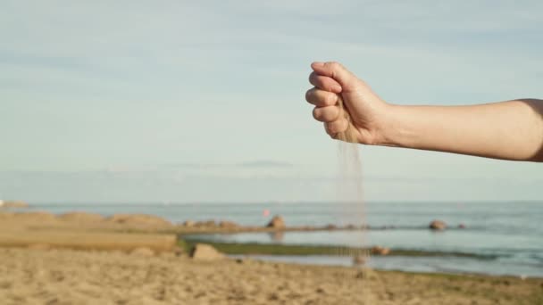 Gimbal Shot of Sand bröckelt aus Frauenhand vor dem Hintergrund von Meer und blauem Himmel — Stockvideo
