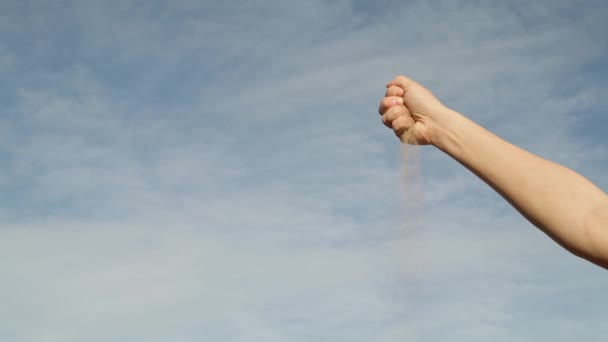 Gimbal shot of woman hand with crumbling sand on sky background — Stock Video