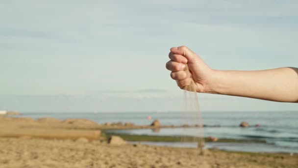 Gimbal slow motion shot of sand crumbling from woman hand on background of sea horizon blue sky — Stock Video