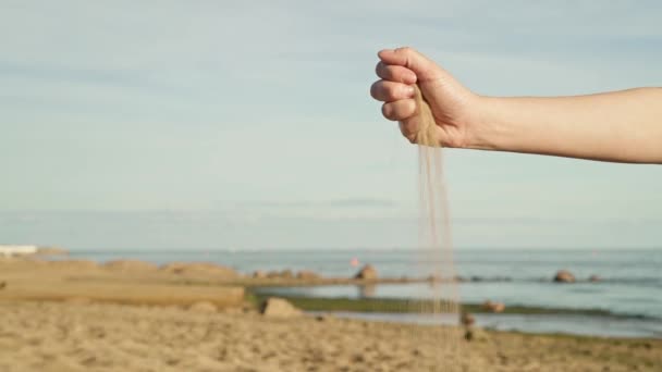 Gimbal schot van zand afbrokkelen van vrouw hand op de achtergrond van de zee en de blauwe lucht — Stockvideo