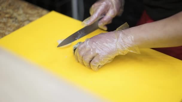 Chef-kok handen snijden een hete sushi rol op een gele tafel — Stockvideo