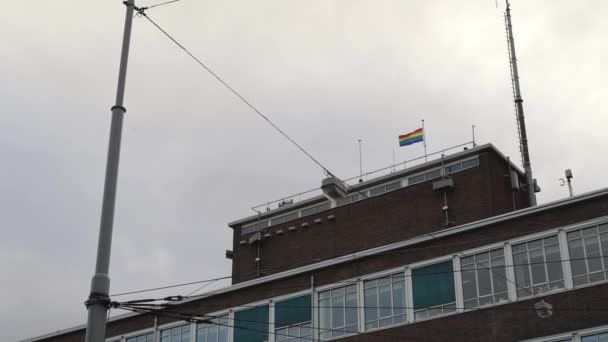 Foto de mano de la bandera lgbt en la parte superior de la casa bajo el cielo gris nublado, la ciudad de Amsterdam — Vídeo de stock