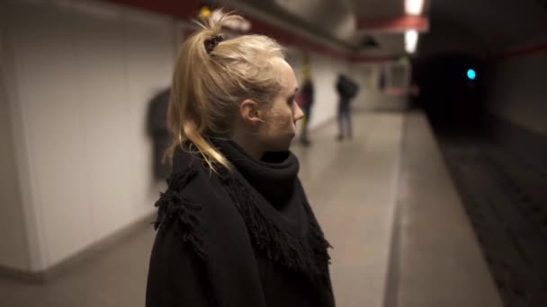 Handgehaltener Mittelschuss einer blonden Frau, die auf U-Bahnsteig steht — Stockvideo