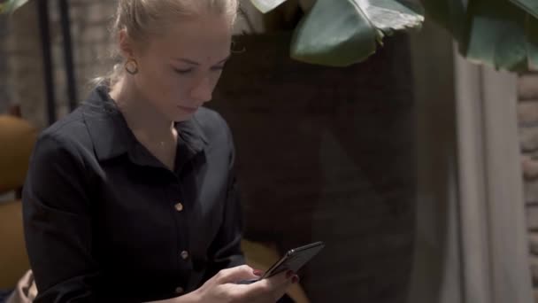 Plano medio de pelo rubio femenino sosteniendo un teléfono, escribiendo — Vídeos de Stock