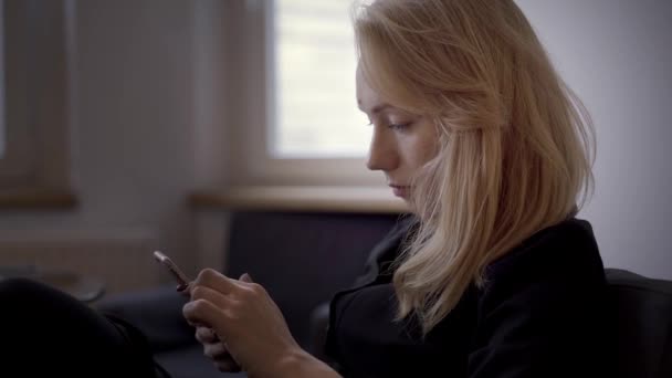 Handheld shot van blonde vrouw zitten sms 'en op de telefoon — Stockvideo