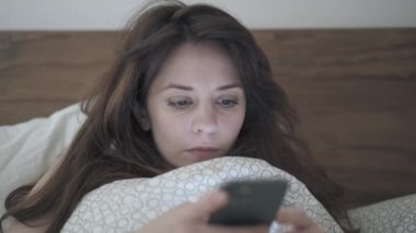Yatakta uzanmış telefonu kaydıran bir kadının el kamerası görüntüsü.