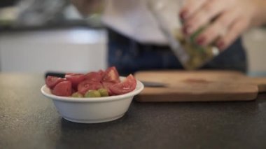 Handheld shot of woman adding olives to the salad with tomatoes