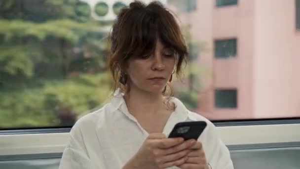 Portrait of attractive caucasian woman in KL monorail using smartphone chatting with friends and browsing the internet. The concept of social networking all day long. Kuala Lumpur on background. — Stock Video