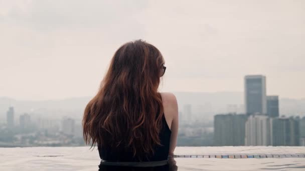 Ein Mädchen chillt am Pool in Kuala Lumpur. Das Konzept der Erholung und des Urlaubs mit dem KL-Stadtblick. — Stockvideo