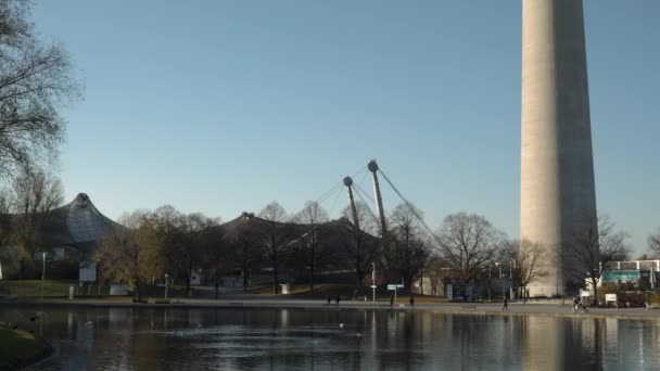 MUNICH - NOVEMBRO 21: Esquerda para a direita pan tempo real estabelecer tiro de um lago no Parque Olímpico em Munique, perto da torre olímpica e do estádio, 21 de novembro de 2018 em Munique, Alemanha . — Vídeo de Stock